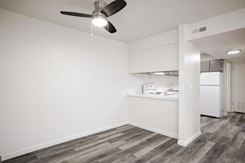 An empty living room with a kitchen and a ceiling fan